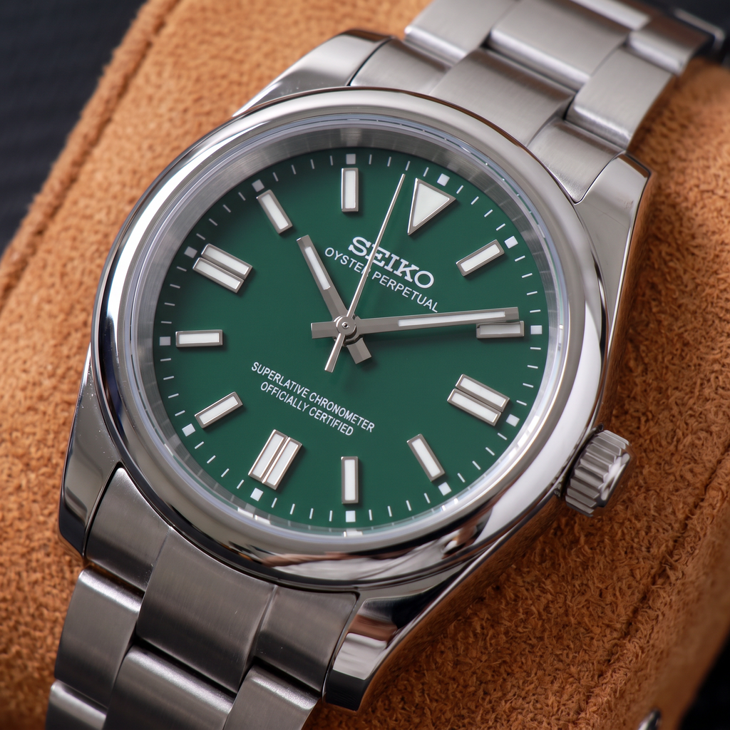 ORA Classic Sport-Style 36mm Seiko Mod watch, emerald green dial, smooth polished bezel, steel three-link bracelet – angled view on a tan suede watch pillow