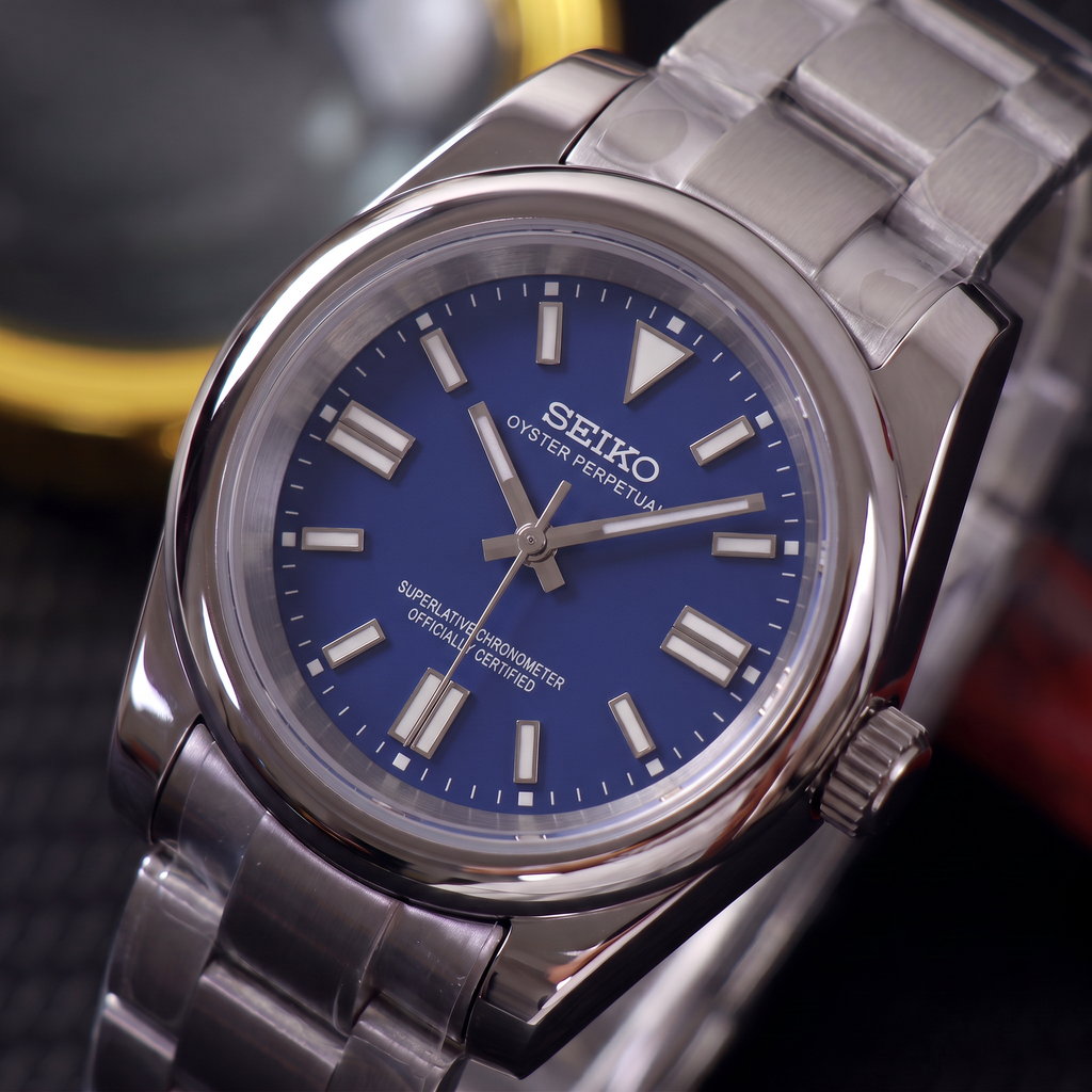 ORA Classic Sport-Style 36mm Seiko Mod watch, cobalt blue dial, smooth polished bezel, steel three-link bracelet – angled view against warm bokeh lights