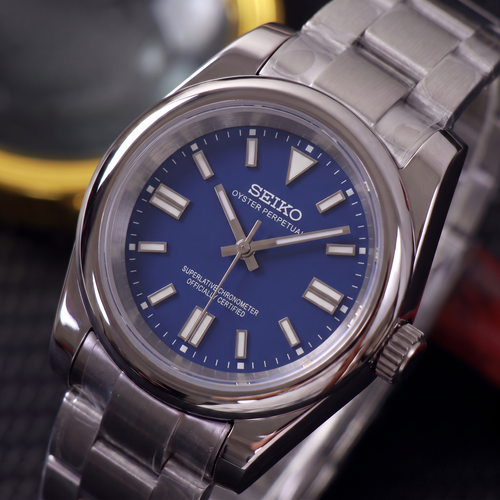 ORA Classic Sport-Style 36mm Seiko Mod watch, cobalt blue dial, smooth polished bezel, steel three-link bracelet – angled view against warm bokeh lights
