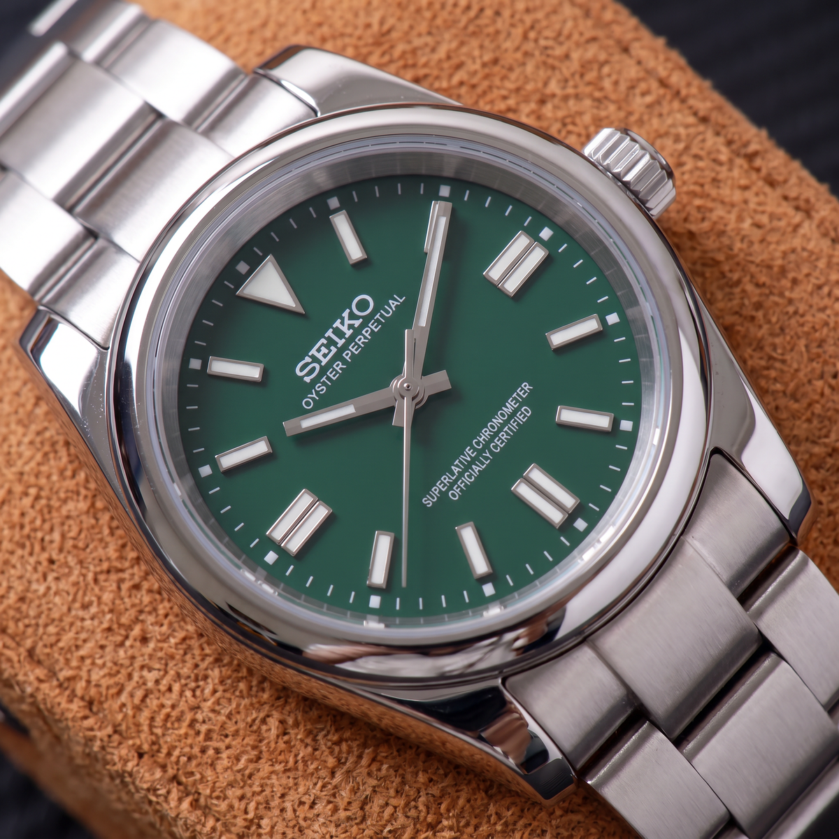 ORA Classic Sport-Style 36mm Seiko Mod watch, emerald green dial, smooth polished bezel, steel three-link bracelet – close-up on a tan suede watch pillow