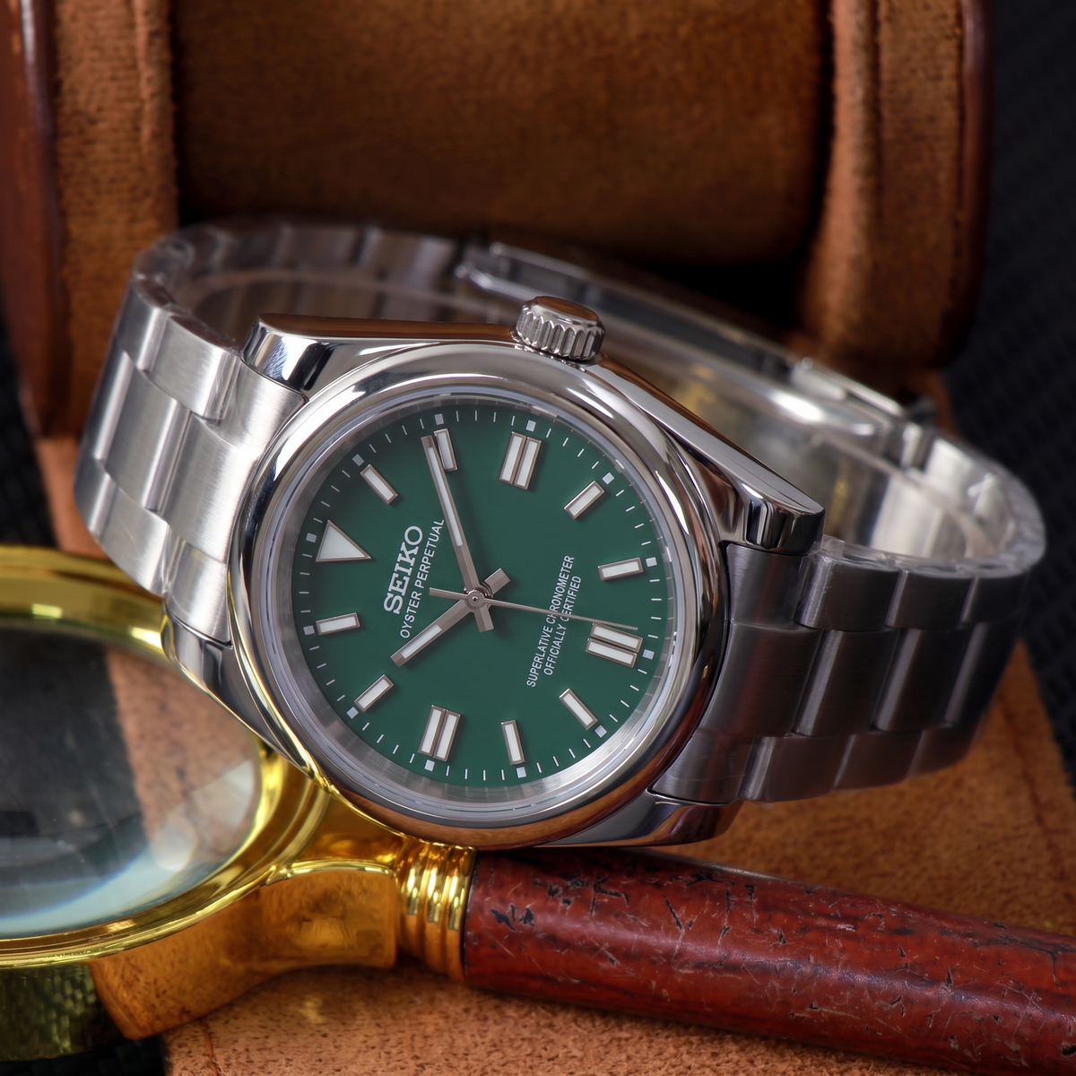 ORA Classic Sport-Style 36mm Seiko Mod watch, emerald green dial, smooth polished bezel, steel three-link bracelet – in a leather watch box beside a brass magnifying glass