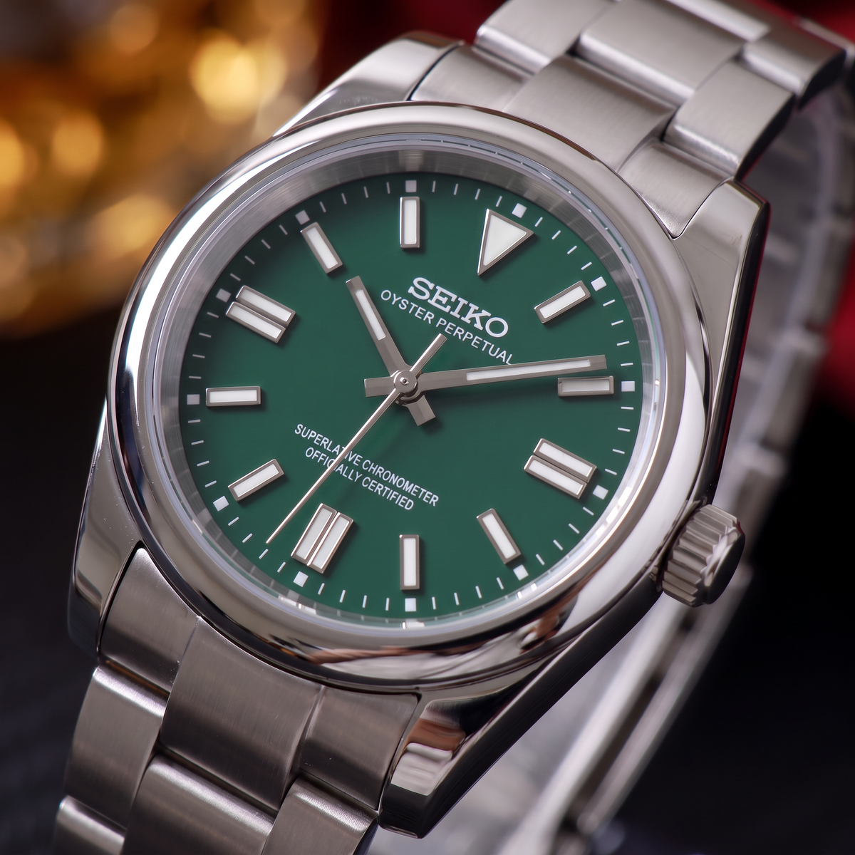 ORA Classic Sport-Style 36mm Seiko Mod watch, emerald green dial, smooth polished bezel, steel three-link bracelet – front view against warm bokeh lights