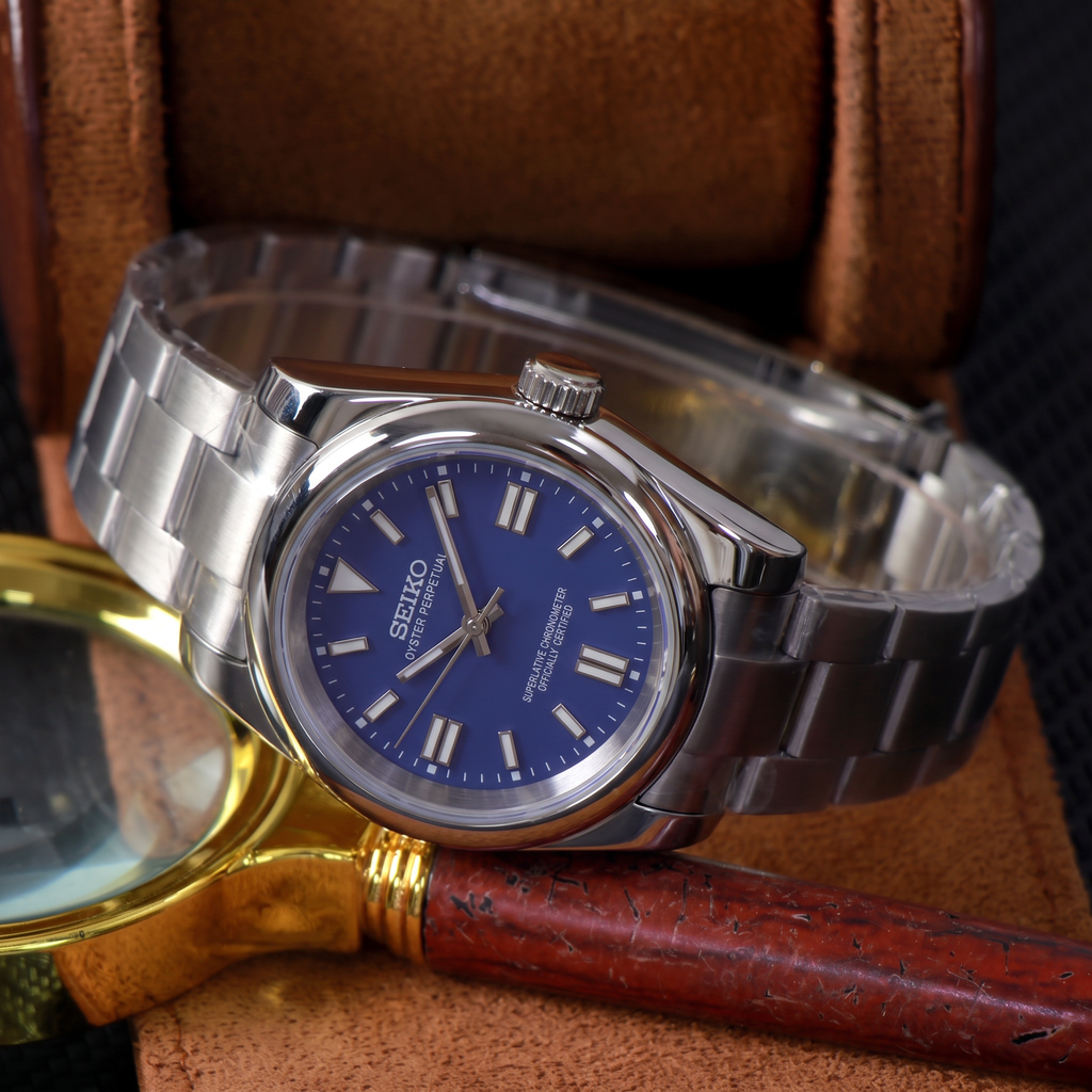 ORA Classic Sport-Style 36mm Seiko Mod watch, cobalt blue dial, smooth polished bezel, steel three-link bracelet – in a leather watch box beside a brass magnifying glass
