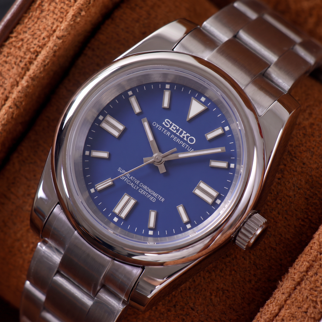 ORA Classic Sport-Style 36mm Seiko Mod watch, cobalt blue dial, smooth polished bezel, steel three-link bracelet – angled view on a tan suede watch pillow