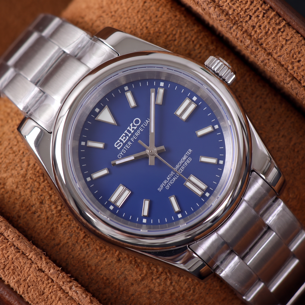 ORA Classic Sport-Style 36mm Seiko Mod watch, cobalt blue dial, smooth polished bezel, steel three-link bracelet – close-up on a tan suede watch pillow