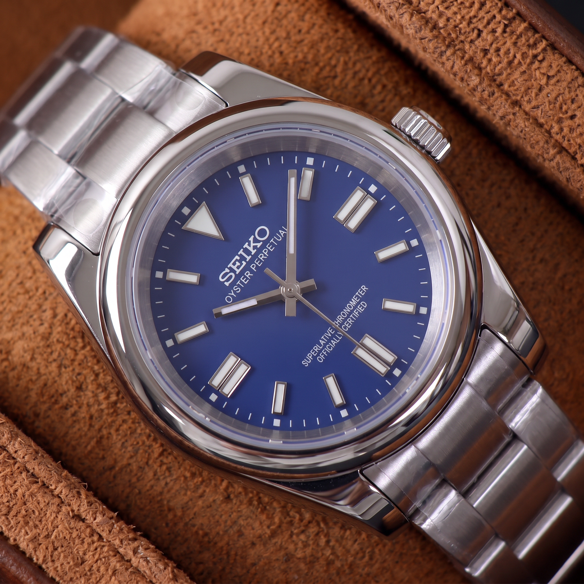 ORA Classic Sport-Style 36mm Seiko Mod watch, cobalt blue dial, smooth polished bezel, steel three-link bracelet – close-up on a tan suede watch pillow