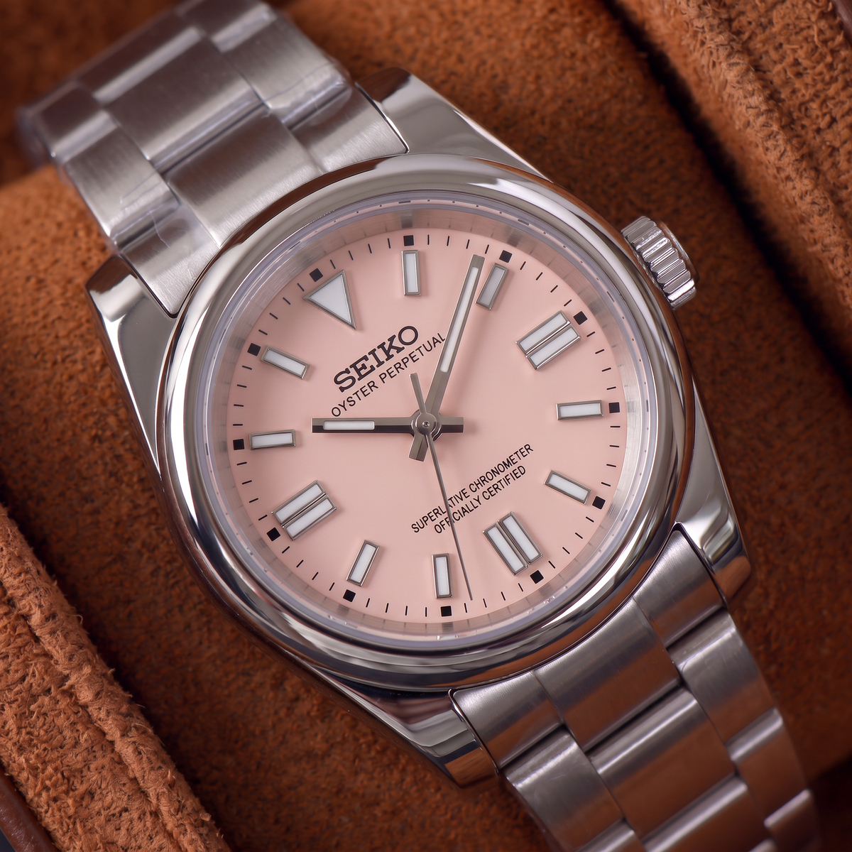 ORA Classic Sport-Style 36mm Seiko Mod watch, blush pink dial, smooth polished bezel, steel three-link bracelet – close-up on a tan suede watch pillow