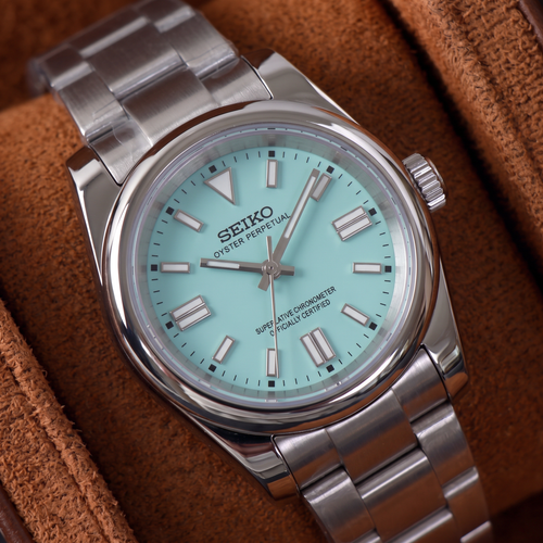 ORA Classic Sport-Style 36mm Seiko Mod watch, aqua dial, smooth polished bezel, steel three-link bracelet – close-up on a tan suede watch pillow